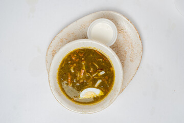 Flavorful green soup garnished with lemon slices, accompanied by a creamy dip on a plate