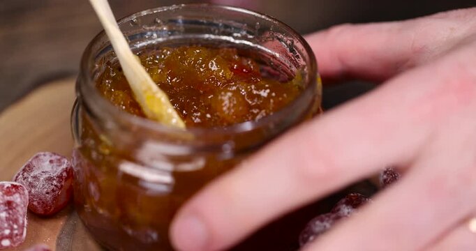 orange jam made from oranges and citrus fruits and dried in sugar syrup, whole kumquat fruits in white sugar , a glass jar with sweet orange jam is on the table