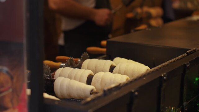 Traditional trdelnik pastry rotates and bakes over open coals at street food market. Process of baking trdelnik in Prague. Concepts of street food and local cuisine