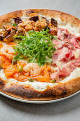 A gourmet pizza features shrimp, salmon, prosciutto, and fresh greens, showcasing vibrant toppings