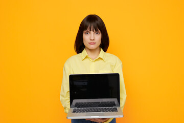 Young woman stands upfront with a laptop extended toward the camera against a bright orange background, presenting a clean, modern tech inspired portrait.