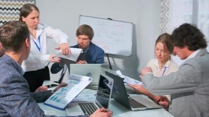 A diverse group of professionals engaged in a project discussion in a modern office setting. Men and women reviewing charts, working on laptops, analyzing documents together during a business meeting. - Powered by Adobe