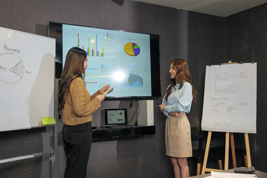 Two business women meet, busy team people collaborate on project work during business meeting, presenting data charts, sharing ideas, planning success in conference room setting