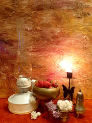 Kerosene lamp, lilac flowers, strawberries. Evening romantic still life on a red background, candle in a candlestick. Romance, flowers, elegance, flair. Antique brass items