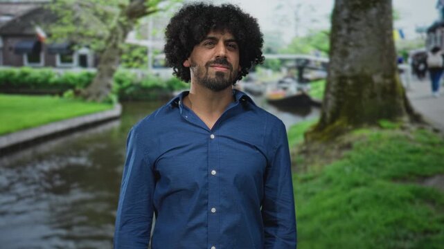 Man with curly hair and beard covers ears with hands on a street by an amsterdam canal next to a tree; frustration noise sensitivity.