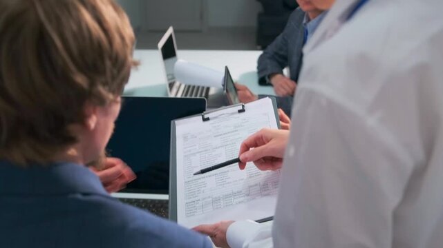 Female assistant interrupts a tense office meeting to get a document signed by the team leader. Group of professionals working under deadline pressure. Business stress and multitasking.