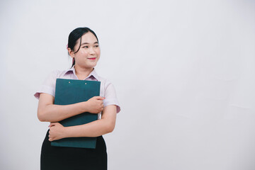Confident young woman with a clipboard standing against a simple white background, showcasing a professional and optimistic attitude in a workplace environment