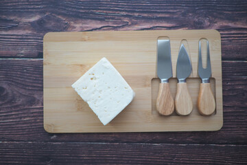 Cheese block and knives on wooden cutting board