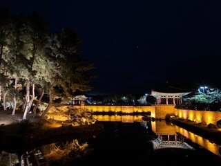 Fototapeta premium Illuminated night view of Donggung Palace and Wolji Pond in Gyeongju, South Korea, showcasing traditional Korean architecture, glowing reflections on calm water, and a serene historic landscape