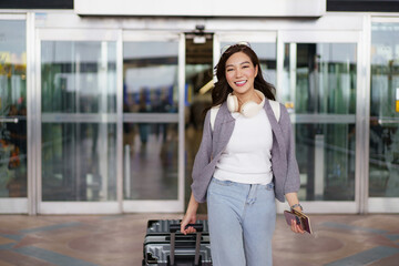 Asian woman waving with passport while entering airport for travel.