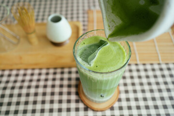 Barista pouring matcha into iced milk to make a layered matcha latte.