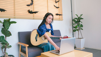 Female Musician Playing Acoustic Guitar While Using Laptop in Modern Indoor Space with Simple Decor and Creative Atmosphere