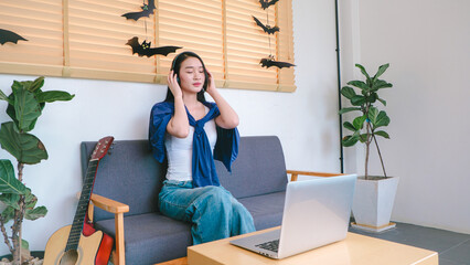 Young Woman Enjoying Music at Home with Laptop Surrounded by Decorative Bats and Indoor Plants Creating a Cozy Atmosphere in a Modern Living Space
