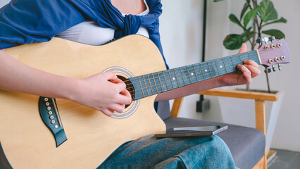 Woman Playing Acoustic Guitar in a Cozy Indoor Setting with Natural Light and Comfortable Furniture