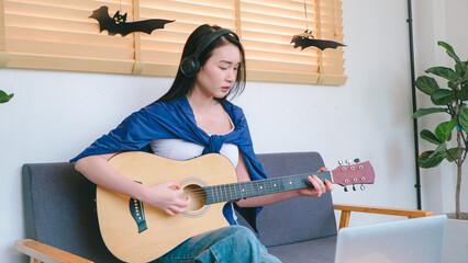 Young Woman Playing Acoustic Guitar in Cozy Indoor Setting with Creative Decorations and Natural Light
