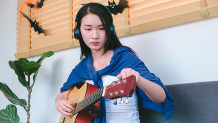 Young Woman Playing Acoustic Guitar Indoors with Headphones and Cozy Atmosphere Surrounded by Halloween Decorations and Plants