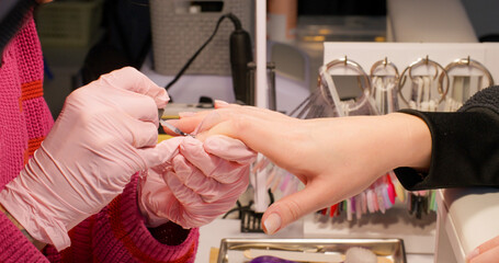 Gel nails. Professional manicure procedure. Female hand in gloves getting cover treatment with acrylic nude polish by beauty technician in salon.