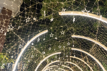 A curved tunnel lined with warm lights glows softly in the dark, and the illuminated arches guide the walkway through a quiet night scene.