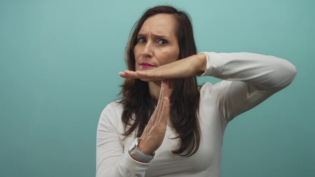 Woman gesturing timeout with serious expression against isolated blue background signifies pause and contemplation.