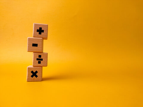 The image displays four wooden blocks with basic mathematical operation symbols on a yellow background