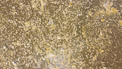 Aerial view of drifting sediment and organic debris forming swirling patterns on river water