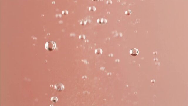 Air bubbles rise through a pink or peach colored liquid on a dark background.&nbsp;This animated movement creates a dynamic and refreshing visual effect.r