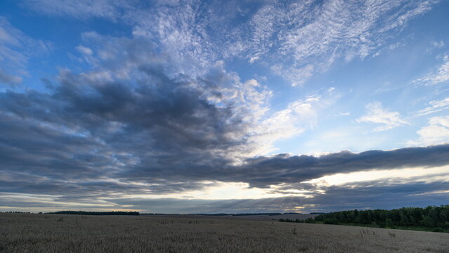Golden sunset panorama, Peaceful sunset scene with colorful clouds and natural surroundings, Vivid evening sky above open plains featuring textured ground and distant trees