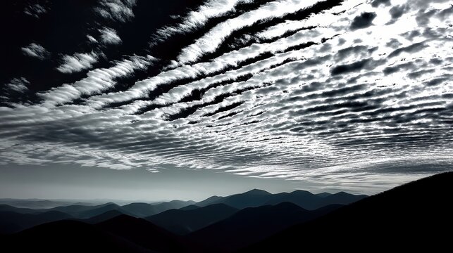 Dramatic altocumulus clouds in a striped pattern stretch across a dark sky above a silhouetted mountain range, creating a moody and atmospheric landscape.