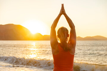Woman practicing yoga on a beach at sunset with mountains in the background