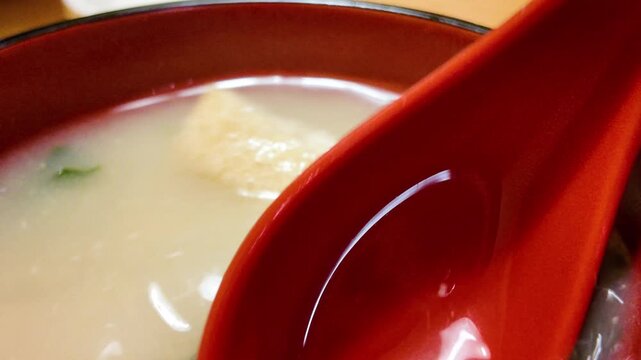 Captivating close-up of a red spoon in a bowl of steaming miso soup containing tofu and green onions, creating a warm and inviting culinary scene.