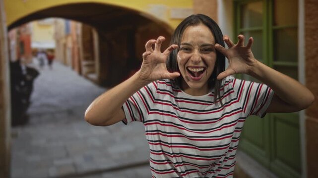 Woman making claw hands and laughing with teeth in a narrow street with a green door; playful joy mischief.