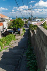 快晴の空とエメラルドグリーンの海の見える街並みと下り坂