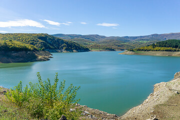 Obraz premium Algeti Reservoir. Emerald blue water with ripples, beautifully curved banks. Hills with green and yellow trees and bushes.