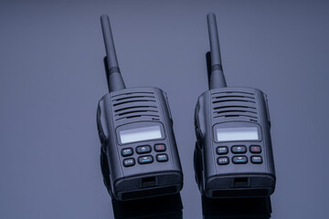 Studio photo of two black walkie-talkies against a black mirror background. High-quality photography of modern walkie-talkie devices. Radio communication for long-range conversations. High quality © Антон Скрипачев