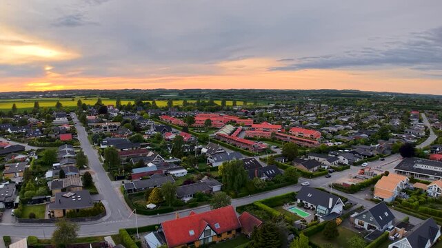 A panoramic aerial drone shot capturing a colorful Danish suburb at sunrise, with rows of houses, streets, and countryside under a dramatic sky.