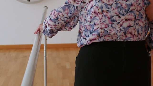 Elderly woman walking on parallel bars with the assistance of a therapist. Mobility and balance rehabilitation in a nursing home. Assisted physical therapy to regain gait and confidence.