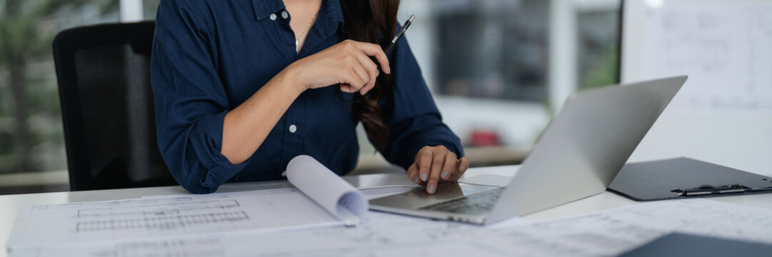 Asian woman architect works on blueprints in a modern office studio - Powered by Adobe