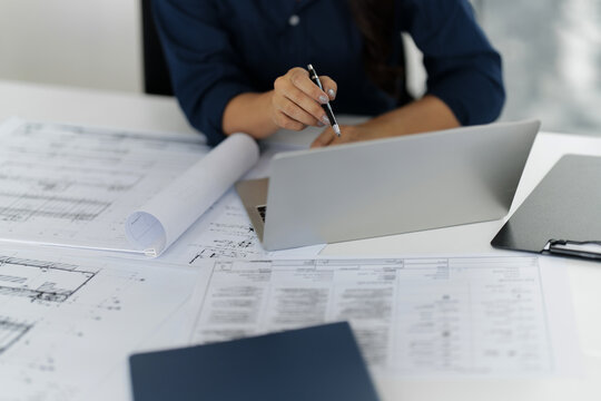 Asian woman engineer designs plans in an office with blueprints