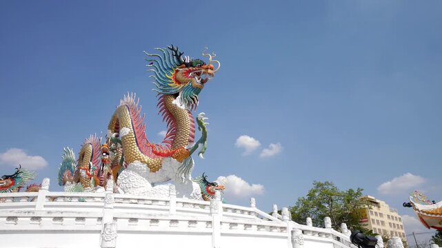 Timelapse of vibrant Chinese dragon statues atop a white temple structure with clouds moving across a bright blue sky in Thailand.