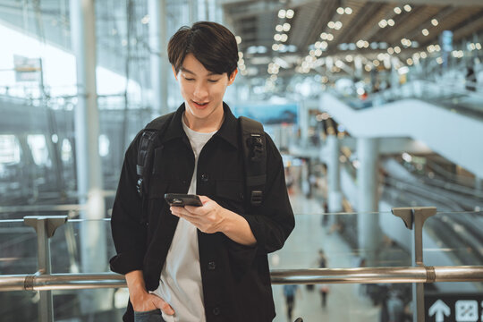Young Asian traveler checking smartphone at airport terminal, modern travel lifestyle, digital boarding, trip planning, technology, journey preparation, vacation mood, millennial traveler at departure - Powered by Adobe