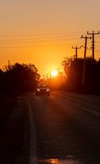 Evening Drive: Car Moving Under Orange Sky and Power Lines