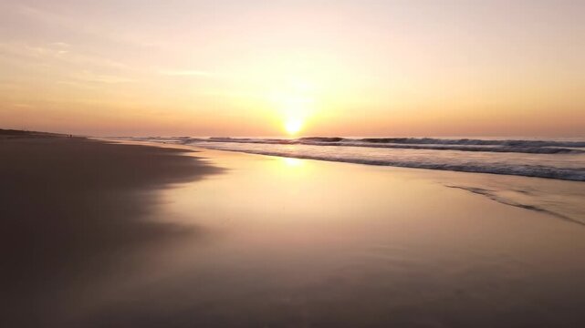 A vibrant summer sunset over the sea with golden sunlight reflecting on ocean waves as the sun nears the horizon by a sandy beach coast under a dramatic sky