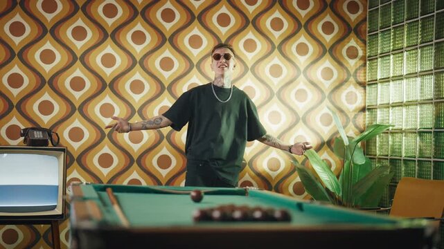 Modern hip-hop singer in retro interior of 70s, extravagant style and fashion. Handsome young man performing rap song, recording music video, tattoos on face and body, contemporary fashion trends