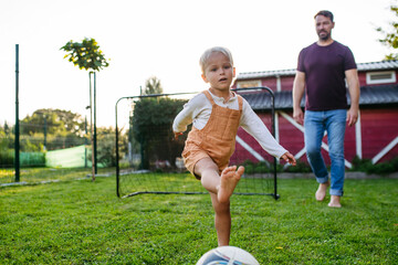 Little boy playing football with father in backyard.