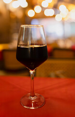 Red wine glass close-up on dining table with warm bokeh background, cozy restaurant ambiance.