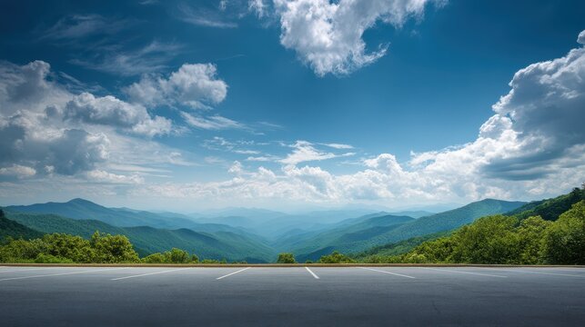 Empty parking lot overlooks layers of green mountains under a vast blue sky with fluffy white clouds, nature landscape