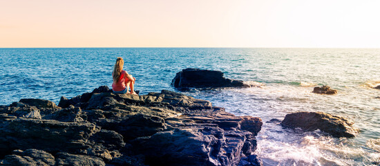 woman sitting on rock looking at the sea. Solitude, loneliness, resilience