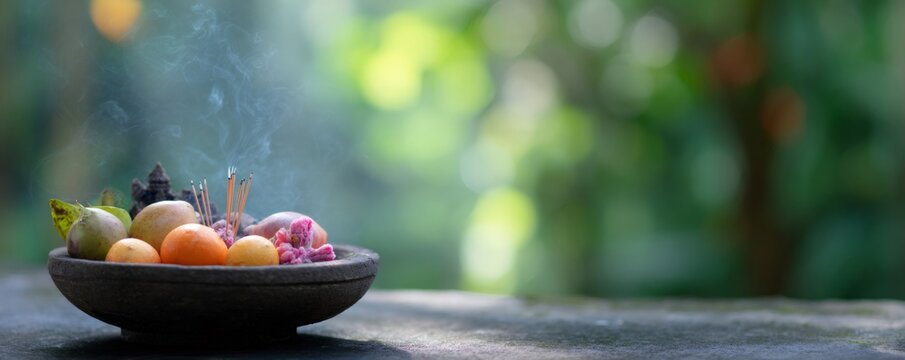 Balinese offering bowl with smoking incense and colorful fresh fruit for daily prayer and ceremonies. Traditional religious ritual in Hinduism. Banner with copy space