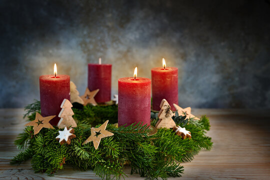 Four red candles on an Advent wreath, three are lit for the third advent, small stars, cinnamon cookies and wooden trees as Christmas decoration, bluish background, copy space - Powered by Adobe