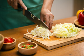 Closeup of male hands slicing Cabbage on a wooden board in the kitchen, preparing to cook.
